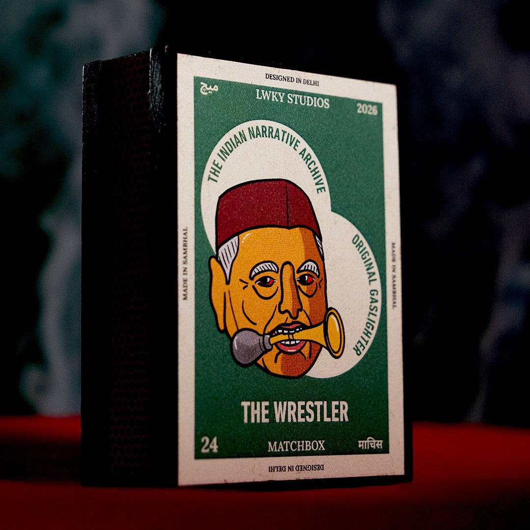 A matchbox-style product box standing upright on a red surface against a dark smoky background. The front label reads 'The Wrestler' and shows a stylized illustrated face with a red hat and gold/yellow details on a green panel.